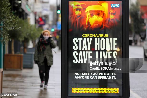 Woman walks past the Government's 'Stay Home, Save Lives' Covid-19 publicity campaign poster in London, as the number of cases of the mutated variant...