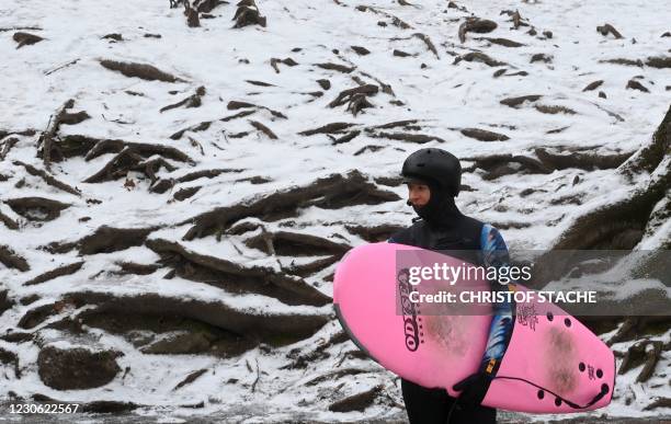 Surfer waits in front of snowy ground near the canal of the Eisbach river at the English Garden park in Munich, southern Germany, during winter...
