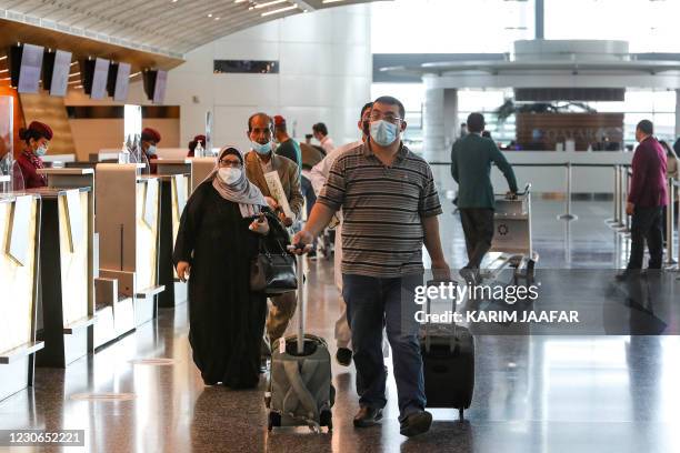 Travellers, mask-clad due to the COVID-19 coronavirus pandemic, walk past the Qatar Airways check-in desk ahead of a flight at Hamad International...