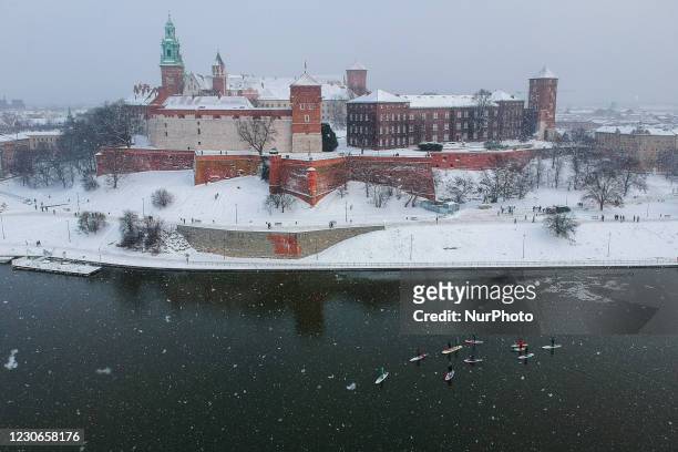An aerial view on Wawel Castle and a group of SUP boarders on Vistula River on a snowy winter day in Krakow, Poland on January 17, 2021....