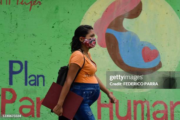 Pregnant woman wearing a face mask walks past a mural "Humanized birth plan" in Caracas, on January 19, 2021. - Talks about legalizing abortion...