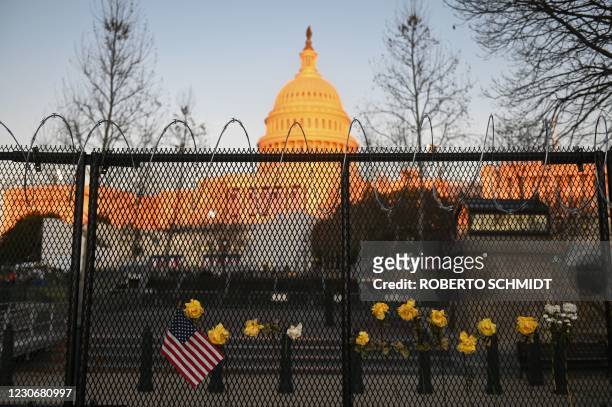 Flag and roses can be seen on a security fence topped by concertina wire surrounding the grounds of the US Capitol Building in Washington, DC on...