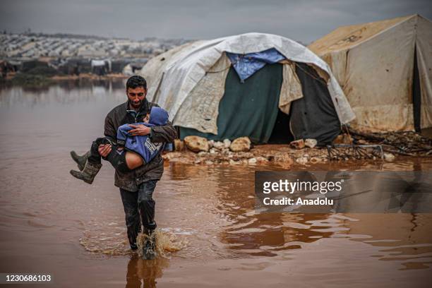 Syrian civilian carries a child as they evacuate their belongings from flooded tents at the Kefer Lusin refugee camp after heavy rain caused floods...