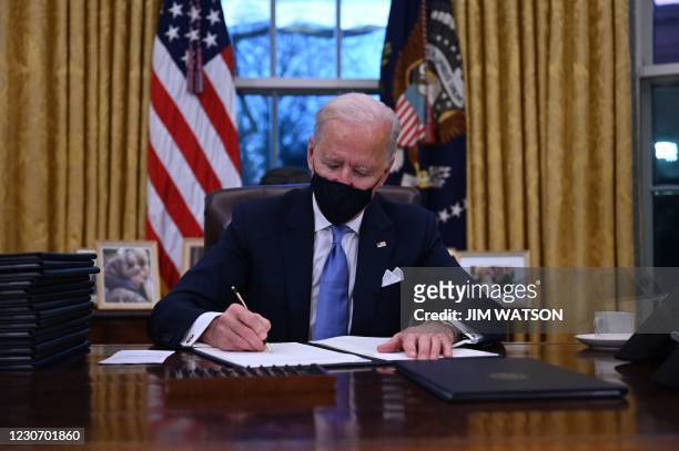President Joe Biden sits in the Oval Office as he signs a series of orders at the White House in Washington, DC, after being sworn in at the US...