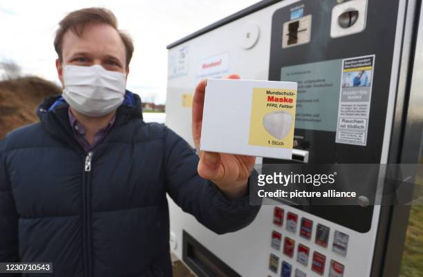 January 2021, Bavaria, Gerolzhofen: Menas Wolf, managing director of Wolf Tabakwaren e.k., holds a pack of FFP2 masks in front of one of his...