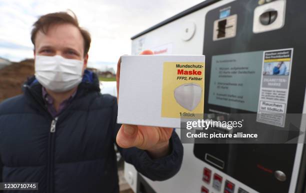 January 2021, Bavaria, Gerolzhofen: Menas Wolf, managing director of Wolf Tabakwaren e.k., holds a pack of FFP2 masks in front of one of his...