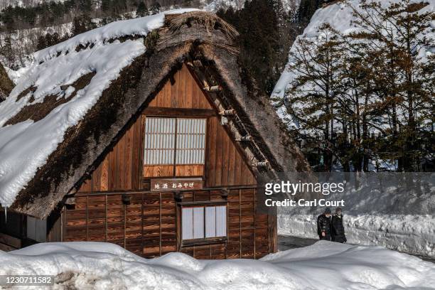 People wearing face masks walk past a traditional building on January 21, 2021 in Shirakawago, Japan. The UNESCO World Heritage-listed village is...