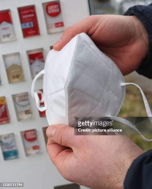 January 2021, Bavaria, Gerolzhofen: Menas Wolf, managing director of Wolf Tabakwaren e.k., holds a respirator mask in his hands in front of one of...