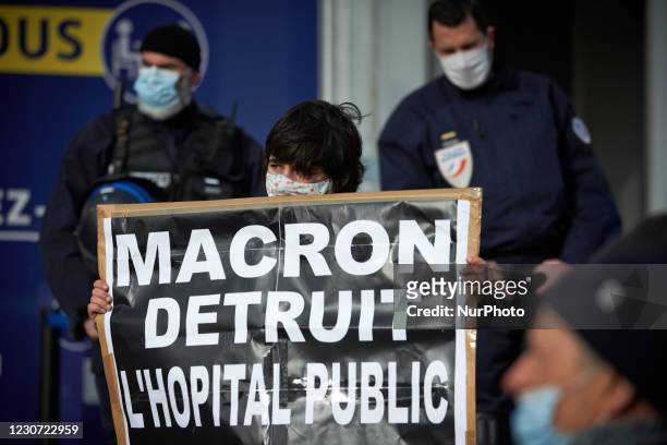Protester holds a cardboardreading 'Macron destroys the public hospital' in front of the entrance of the social Security building guarded by riot...
