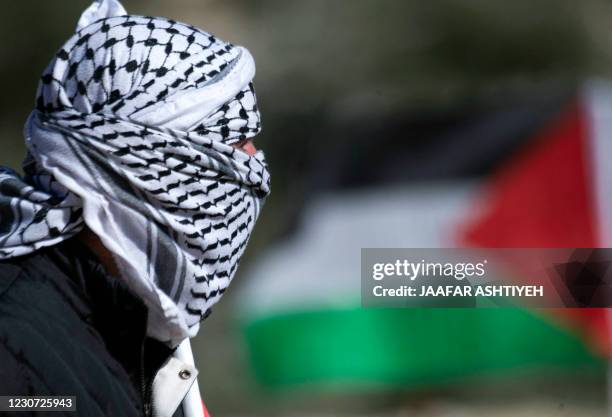 Palestinian protester, masked with a a traditional keffiyeh scarf, looks on amid clashes with Israeli security forces during a demonstration against...