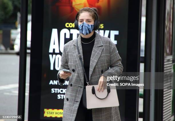 Woman wearing a protective face mask walks in front of an 'Act Like You've got it' warning sign on a London street. England remains under lockdown as...