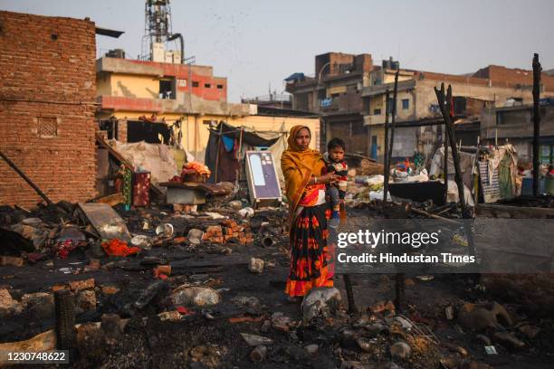 Woman with a child standing among remains of charred homes after a fire that broke out in a slum area at Ghazipur on January 23, 2021 in New Delhi,...