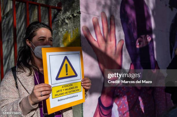 Woman holds a placard reading 'Attention, art and women in danger of extinction' next by a feminist mural named 'Union makes force', during a protest...