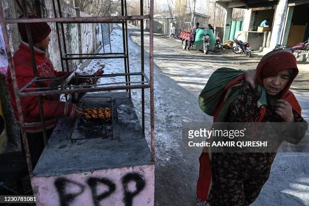 Street vendor prepares food at his stall as a woman walks past in Skardu in the Gilgit-Baltistan region of northern Pakistan on January 25, 2021.