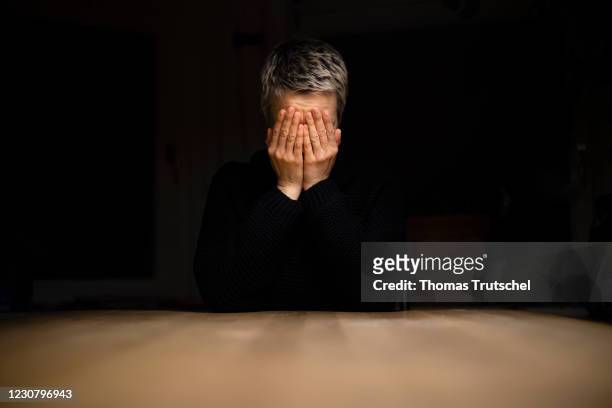 Symbolic photo on the subject of loneliness and depression: A woman sits alone at the table at night and holds her hands in front of her face on...