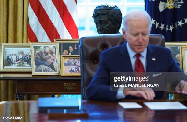 Family photos and a bust of US labor leader Cesar Chavez decorate a table behind US President Joe Biden as he speaks before signing executive orders...