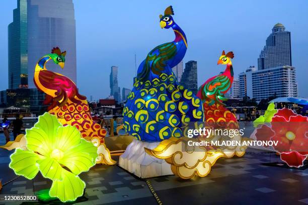 People walk past illuminated paper peacocks installed outside a shopping mall to celebrate the upcoming Lunar New Year in Bangkok on January 29, 2021.