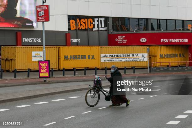 Woman holding a bicycle and wearing a facemask is seen in front of the containers. The Philips Stadion, PSV club stadium in the Dutch city of...