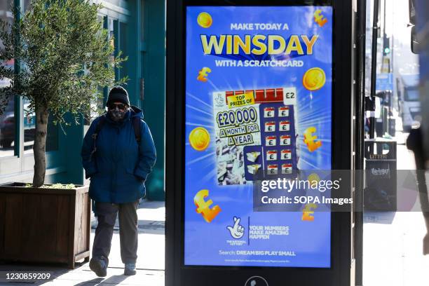 Man wearing a face mask walks past the National Lottery's scratchcard promotion advert in London.