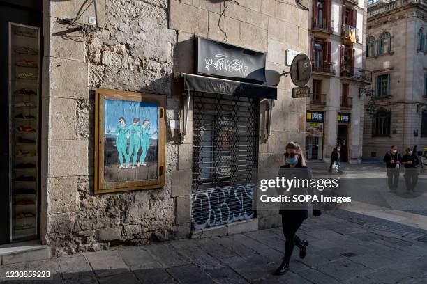 Woman wearing a mask walks past a graffiti of the three vaccines, Moderna, Pfizer and AstraZeneca by TVBoy in Plaza de Sant Jaume. A new graffiti art...