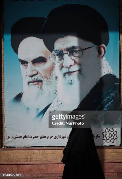 An Iranian veiled woman wearing a protective face mask walks past portraits of Irans Late Leader Ayatollah Ruhollah Khomeini and Supreme Leader...