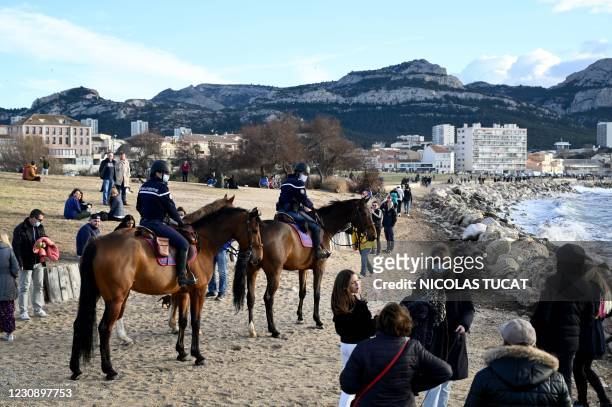 Mounted police offciers patrol as bystanders walk on the seafront in Marseille, southeastern France, on January 31, 2021.