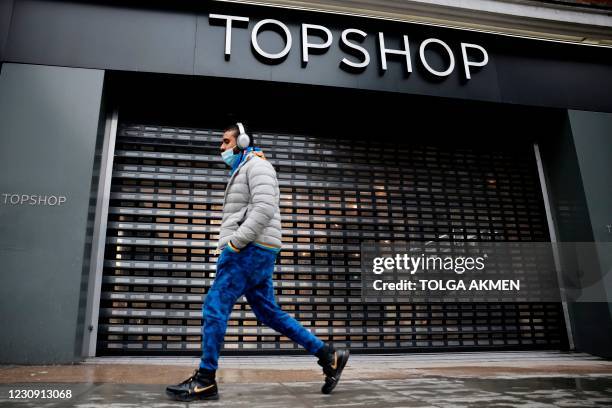 Pedestrian walks past the shuttered entrance of a closed-down Topshop fashion store is pictured trough a window in London on February 1, 2021. -...