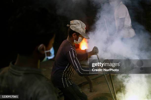 Workers of all ages work together as they prepare to pour molten iron into a mold to make a propeller at a workshop on the bank of the Buriganga...