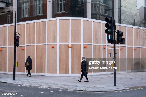Woman wearing a face mask in front of a wooden hoarding surrouding a building on Oxford Street which is empty of shoppers as the national coronavirus...