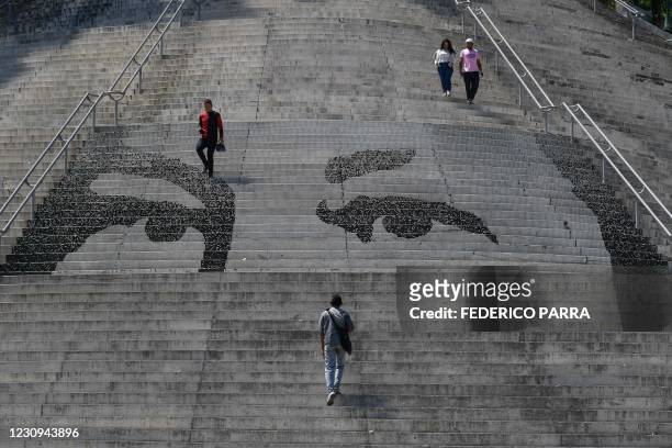People walk by a mosaic portraying the eyes of late Venezuelan President Hugo Chavez on stairs at Calvario Square in Caracas on February 2, 2021. -...