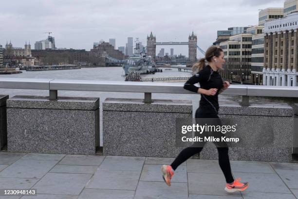 Woman running across London Bridge looking towards Tower Bridge as the national coronavirus lockdown three continues on 28th January 2021 in London,...