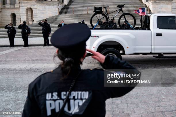 Capitol Police office salutes at attention as a truck carrying the bike of US Capitol Police officer Brian Sicknick departs the US Capitol building...