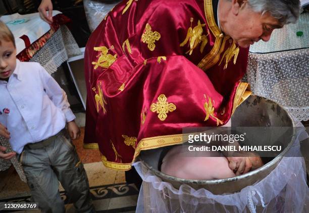 Picture taken on May 11, 2014 shows a Romanian Orthodox priest sinking a child in holy water during baptism, in a church in Bucharest. - Many...