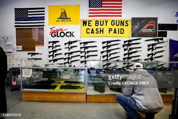 Customer looks at handguns in a case as AR-15 style rifles hang on a wall at Davidson Defense in Orem, Utah on February 4, 2021. - Gun merchants sold...