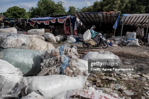 Man rides motorcycle as he carries a sack of plastic trash from the Suwung landfill on January 27, 2021 in Suwung, Bali, Indonesia. In Bali, famed...