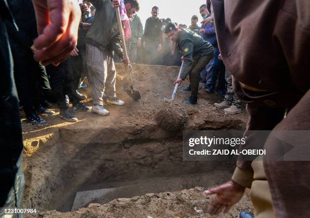 Mourners gather around as a coffin is buried a coffin during a a mass funeral for Yazidi victims of the Islamic State group in the northern Iraqi...