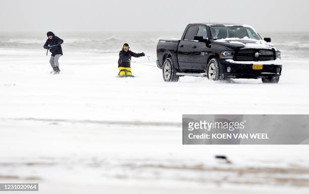 Two boys are pulled on their boards behind a vehicle along the beach of Egmond on February 7, 2021. - The Netherlands is blanketed by the first major...