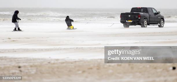 Two boys are pulled on their boards behind a vehicle along the beach of Egmond on February 7, 2021. - The Netherlands was blanketed on February 7,...