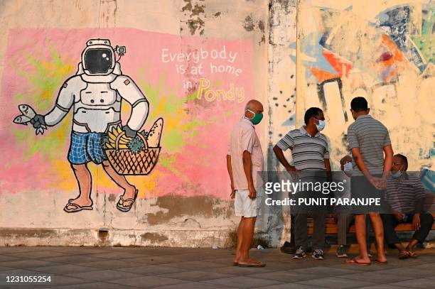People sit near a wall mural in a French colony in Pondicherry on February 9, 2021.