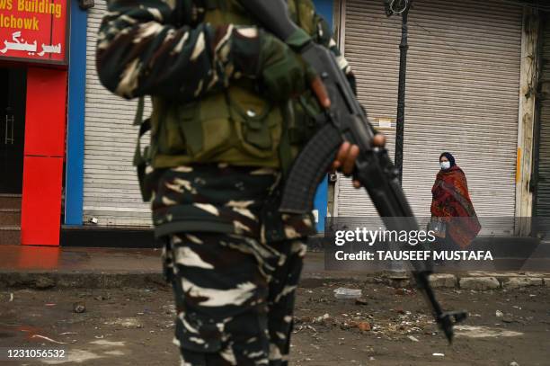 Woman walks past closed shops and an Indian government soldier standing guard during a one-day strike on the death anniversary of Afzal Guru, who was...