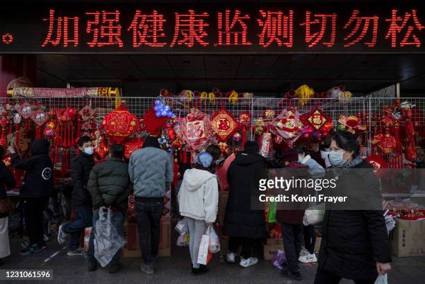 As sign reminds people to not relax health monitoring as shoppers and vendors wear protective masks in a shopping area selling traditional festive...
