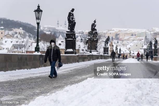 Woman wearing a facemask as a preventive measure against the spread of coronavirus, walks on the iconic Charles Bridge. Heavy snowfall across the...