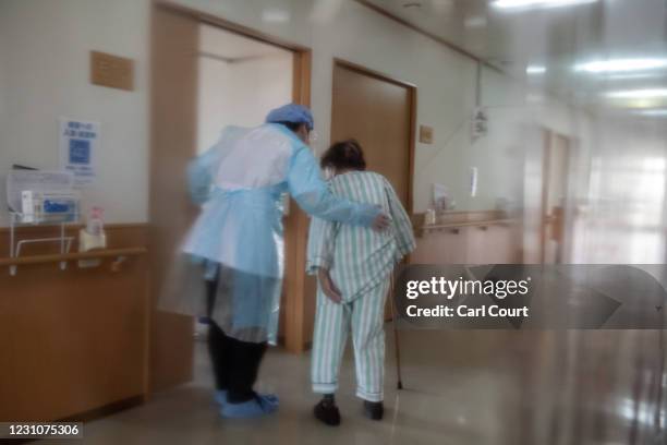 Nurse is pictured through plastic sheeting dividing the sterile and non-sterile areas of a coronavirus ward as he helps an elderly coronavirus...