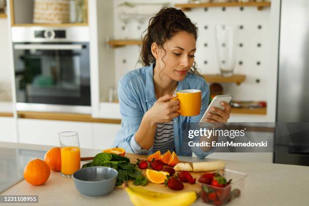 young woman using her mobile phone while preparing fruit smoothie in the kitchen - mixing stock pictures, royalty-free photos & images