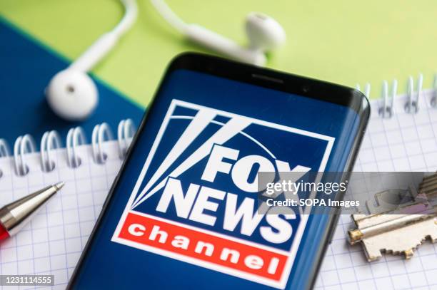 In this photo illustration, a Fox News logo seen displayed on a smartphone with a pen, key, book and headsets in the background.