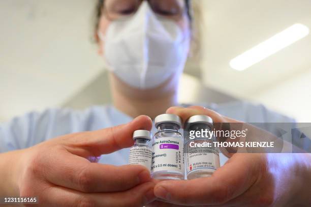 Woman wearing a face mask shows three vials with different vaccines against Covid-19 by Pfizer-BioNTech, AstraZeneca and Moderna in the pharmacy of...