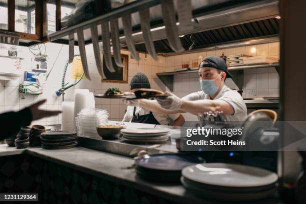 Masked kitchen workers pass finished plates of food to a server at Claro restaurant on February 12, 2021 in New York City. New rules allow...