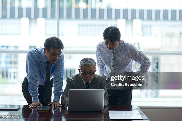 tree businessmen who are looking at personal compu - 職場　日本 ストックフォトと画像