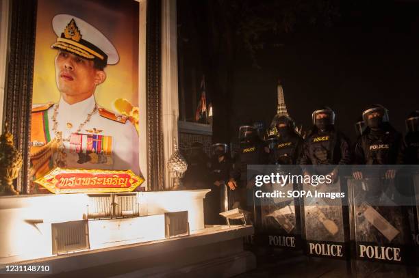 Riot police wearing face masks stand on guard next to a portrait of Thailand King Maha Vajiralongkorn outside the Royal Grand Palace during the...