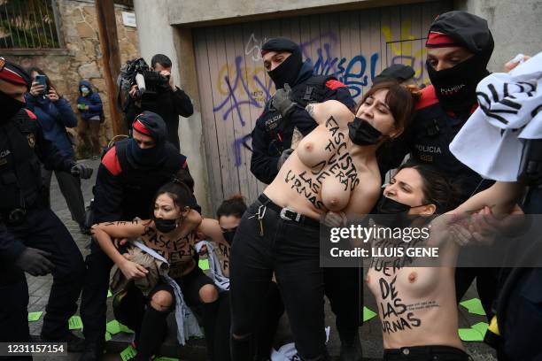 Femen activists with their bare chests reading "Fascists out of ballot boxes" are held back by Catalan regional police forces Mossos d'Esquadra as...